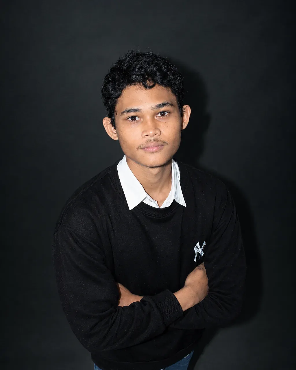 Portrait of Moch Lutfi standing with arms crossed against a dark studio backdrop