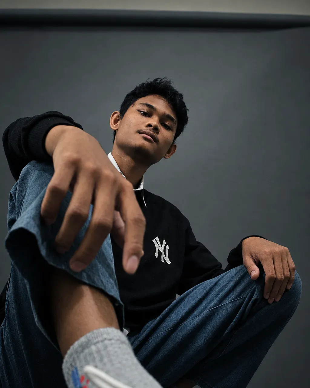 Portrait of Moch Lutfi seated against a grey studio backdrop, hand toward the camera
